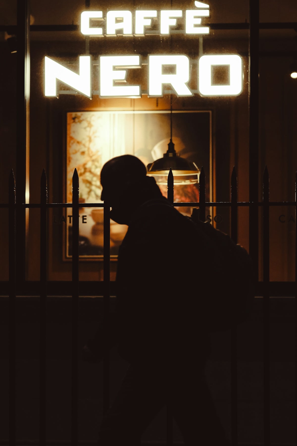Silhouette of person in front of caffè nero at night.