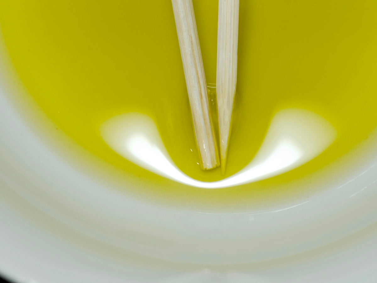Wooden chopsticks dipped into yellow oil in a white bowl.
